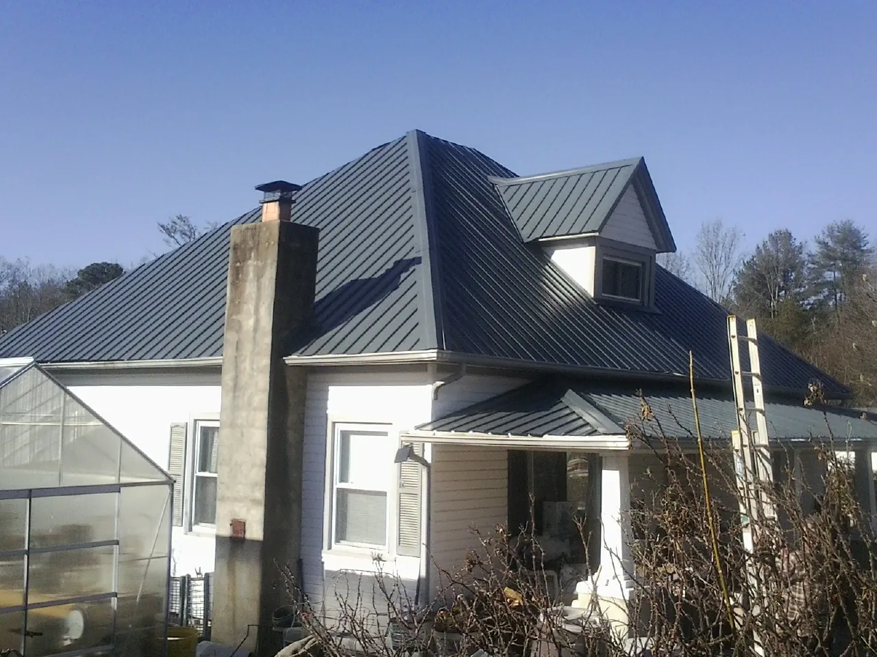 Dark blue standing seam metal roof on a white farmhouse with dormer — Slate & Tile Roof Repair by Roofing Brothers in Roaring River