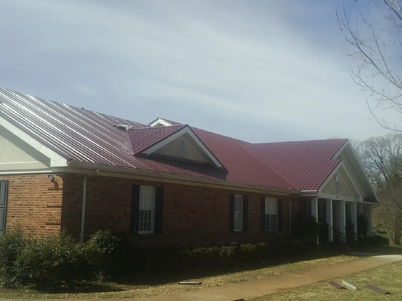 Red metal roof with gabled entries on a long brick building, from a Hail Damage Roof Repair job in Roaring River