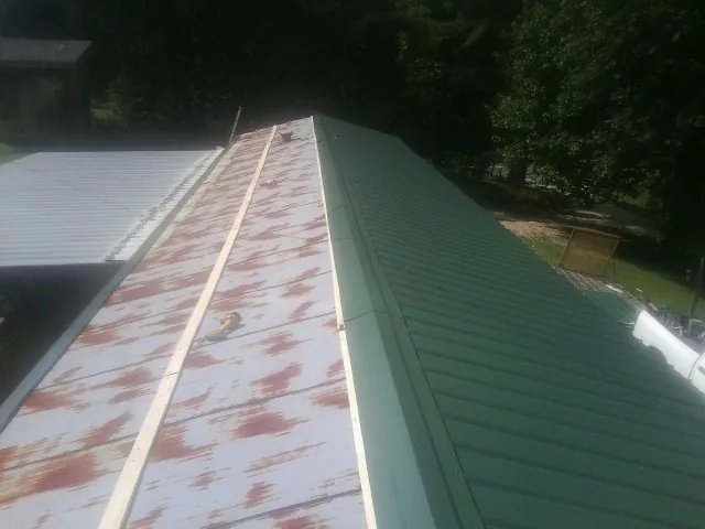 Old rusted panels beside newly installed green metal roofing — Wind Damage Roof Repair by Roofing Brothers in Roaring River