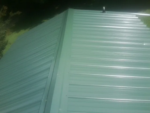 New green metal panels meeting at the ridge of a roof — Flat Roof Repair work by our crew in Roaring River