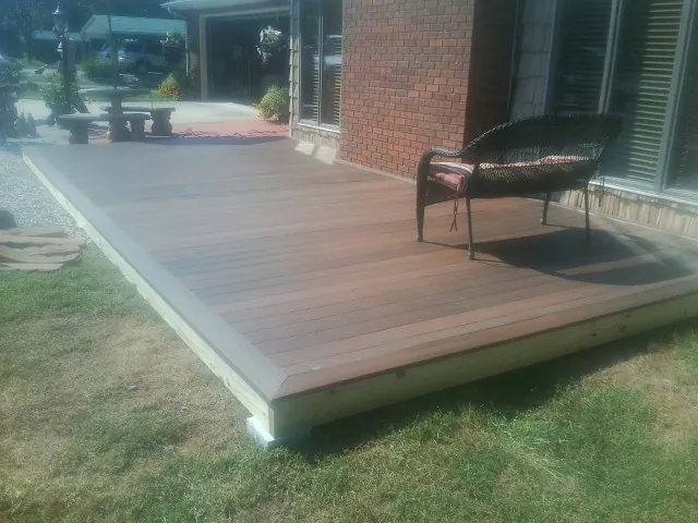 New wood deck and wicker chair beside a brick house in Roaring River