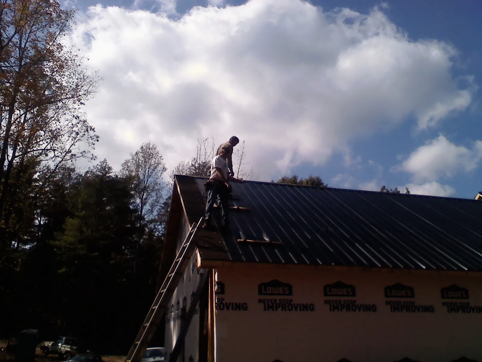 Roofer fastening dark metal panels high against a cloudy sky, from a Roof Inspection job in Roaring River
