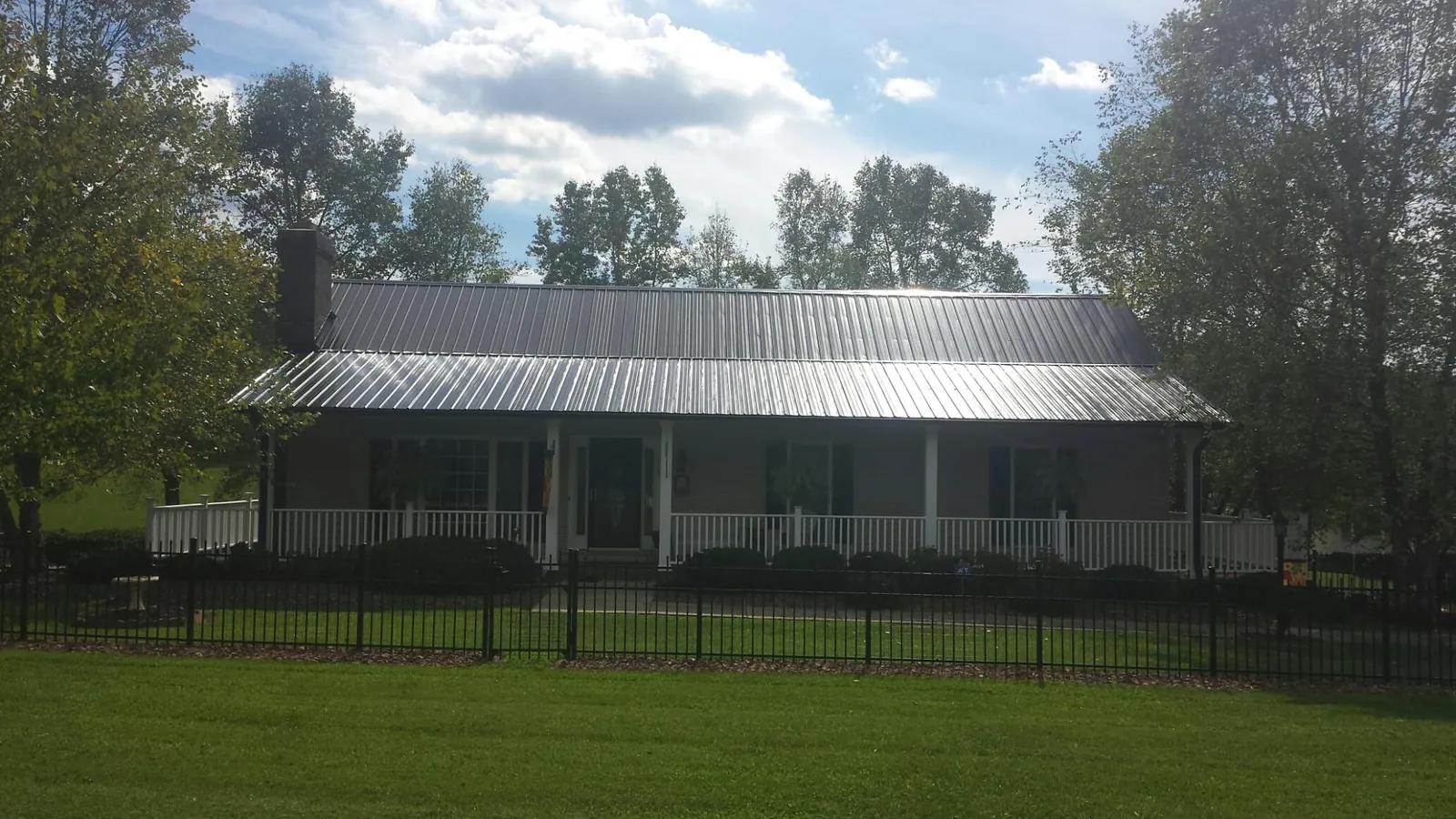 Gray metal roof on a brick ranch with a full width front porch — Gutter Guard Installation work by our crew in Roaring River