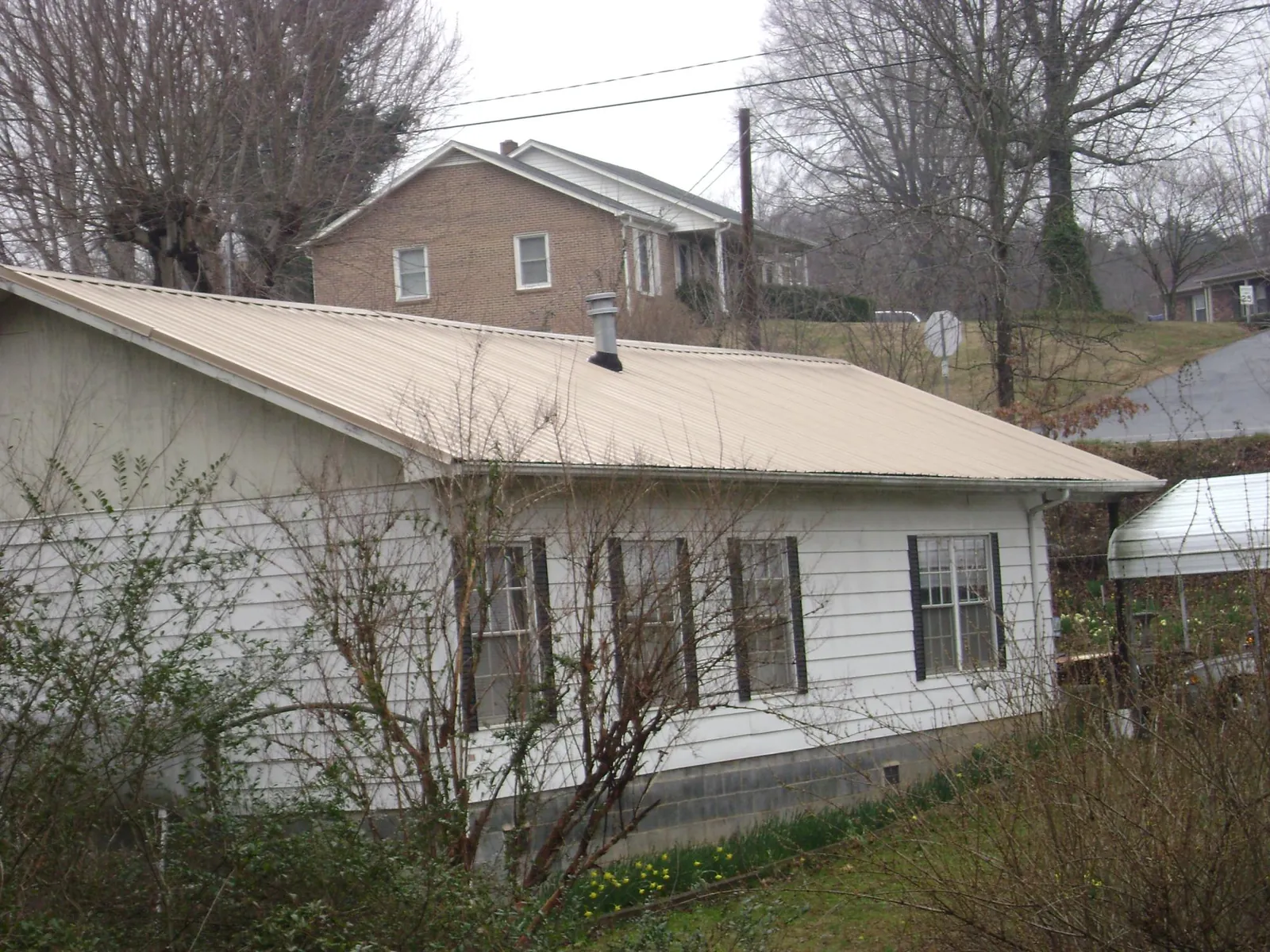 Tan metal roof on a white sided house set into a hillside — Commercial Roofing by Roofing Brothers in Roaring River