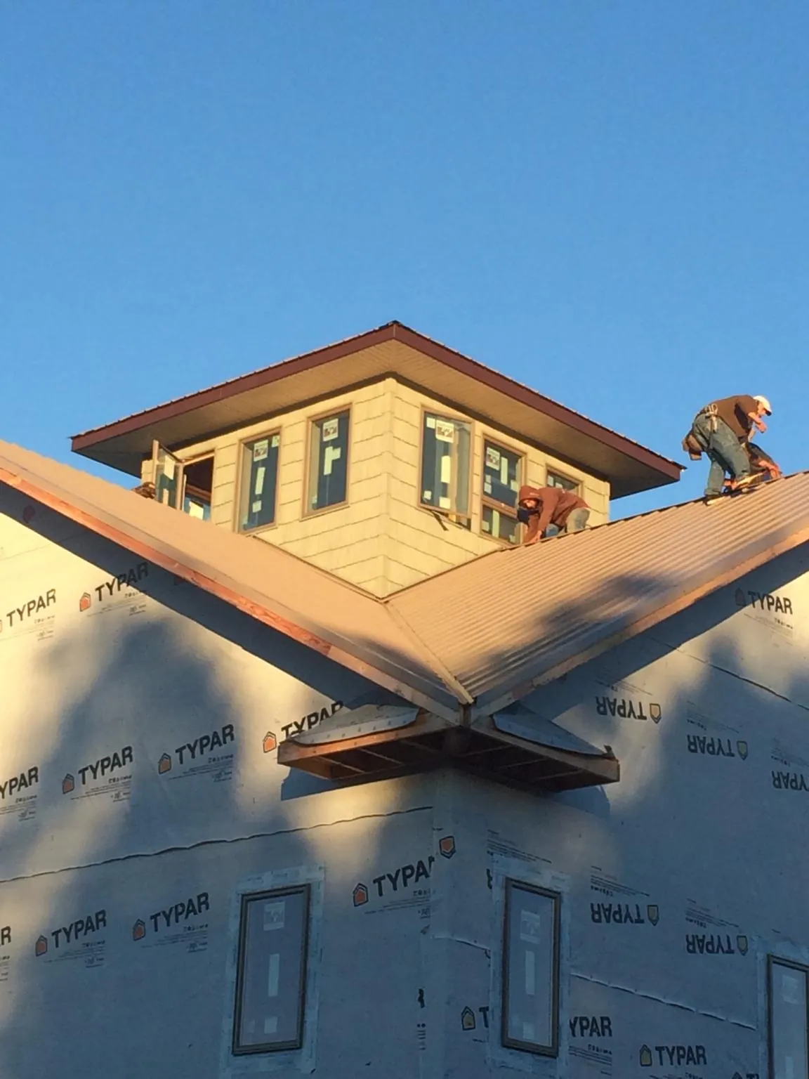Roofers working around a rooftop cupola on a new metal roof at sunset — Roof Waterproofing in Roaring River by Roofing Brothers